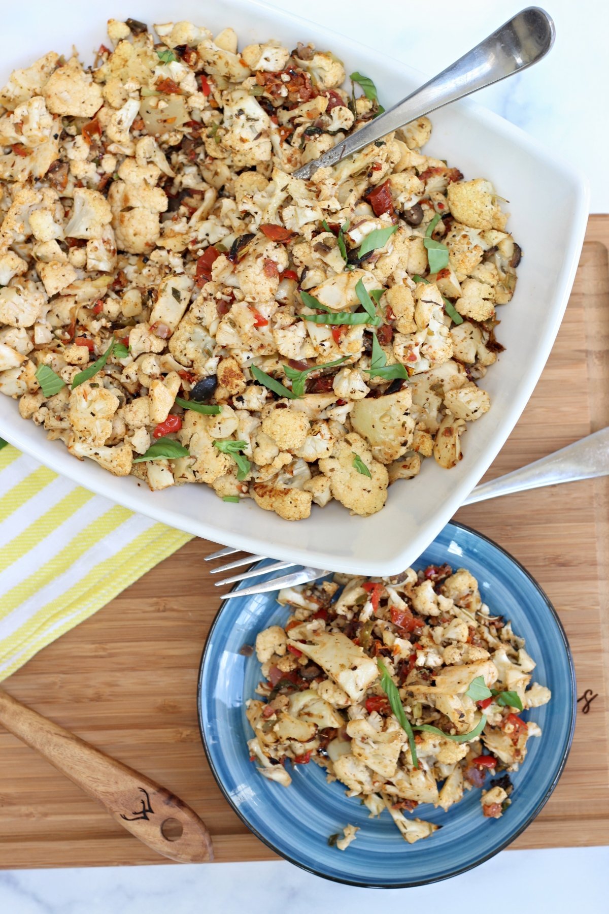 Roasted cauliflower florets with peppers and onions in a white casserole, garnished with herbs.