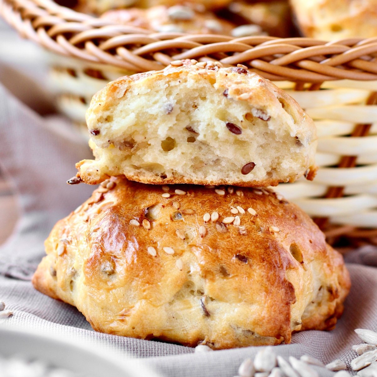 Golden-brown seeded bread rolls stacked, one half showing a soft, crumb-filled interior with sesame seeds on top.