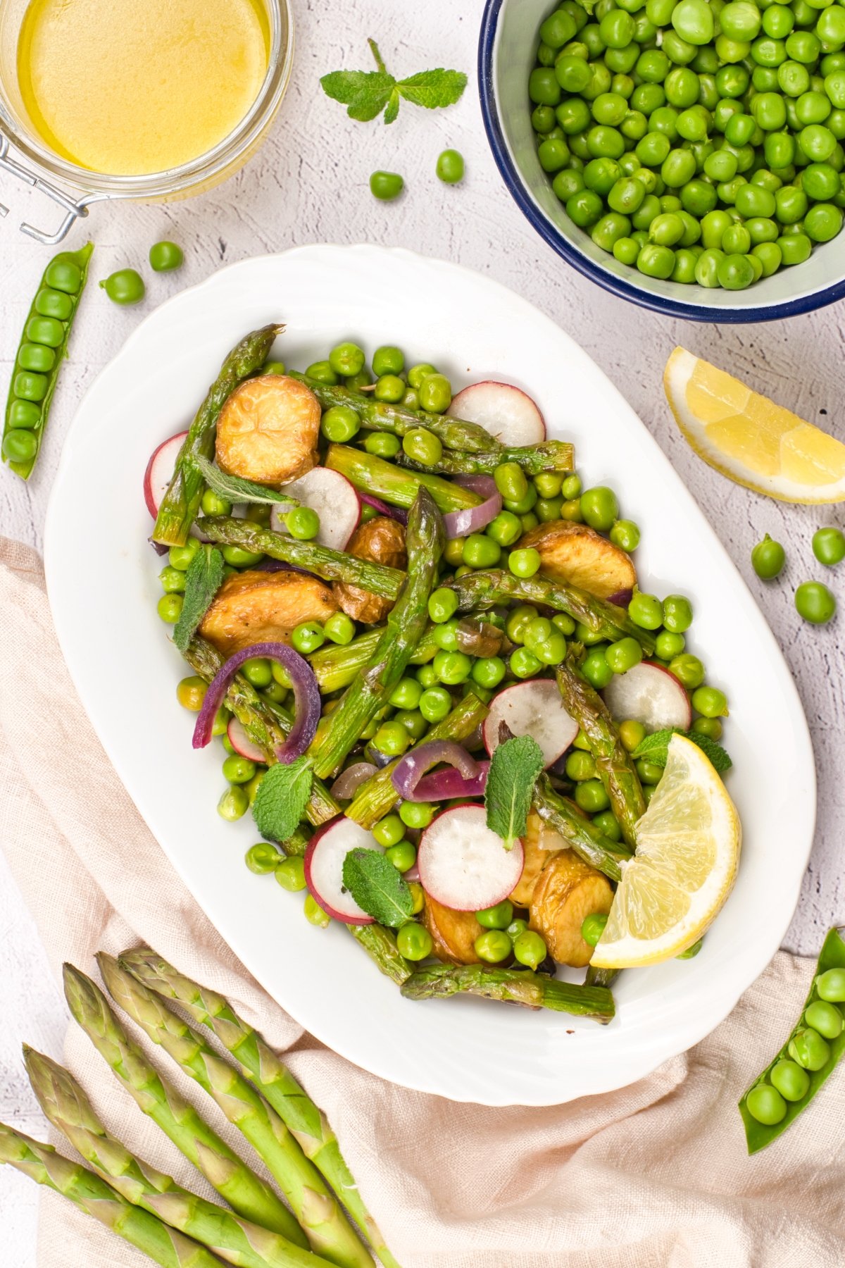 Plate of roasted asparagus, peas, radishes, and lemon wedges on a white platter with mint garnish, ready for serving